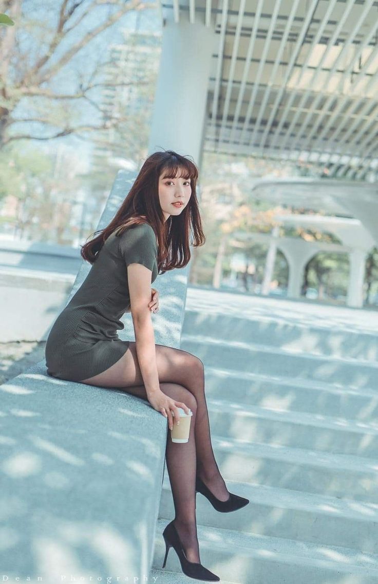 Woman in a short dress and black pantyhose sitting outdoors with a cup