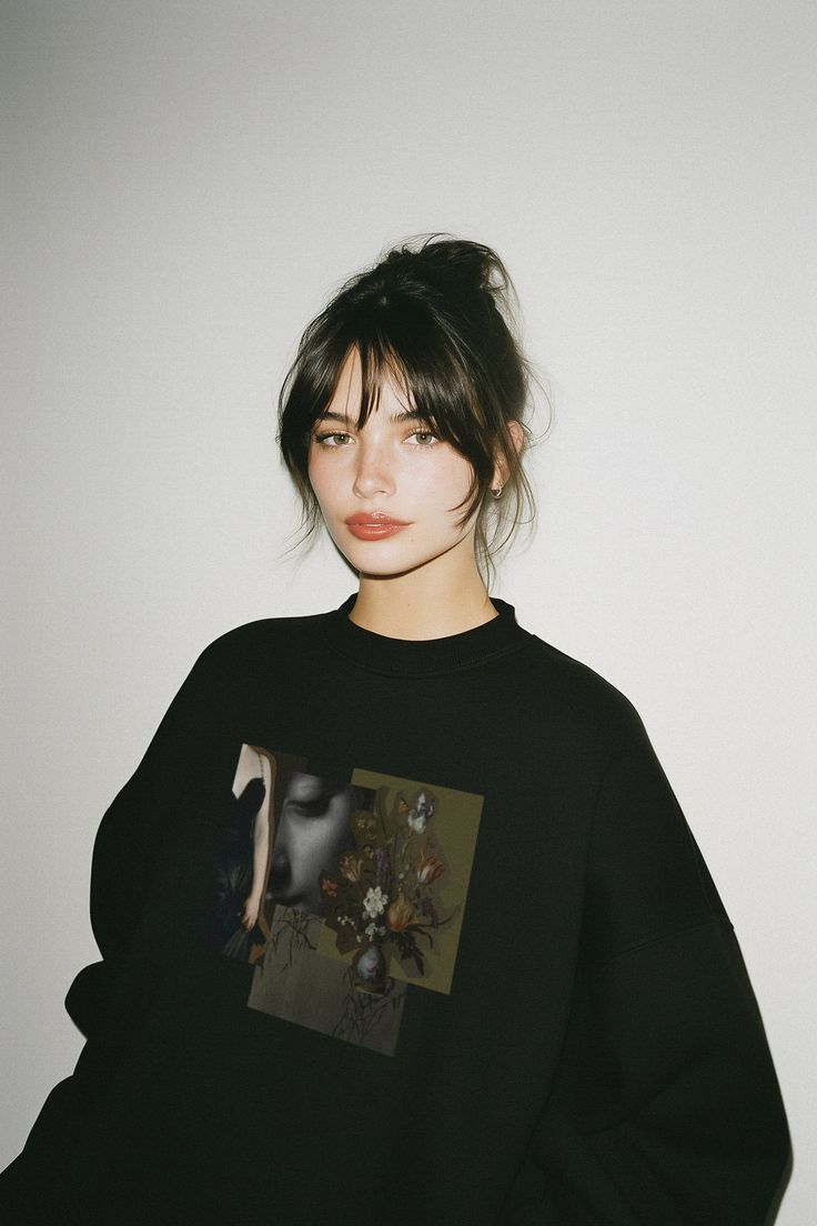 Woman with dark hair and bangs wearing a black sweatshirt with a graphic print