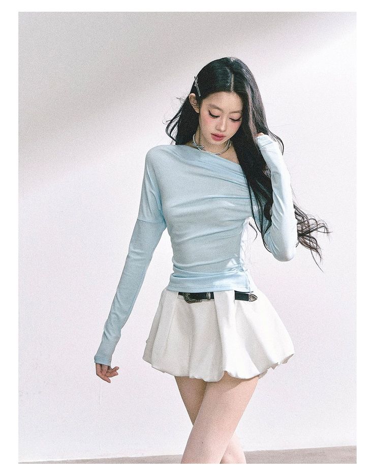 Woman with long black hair wearing a light blue top and white mini skirt