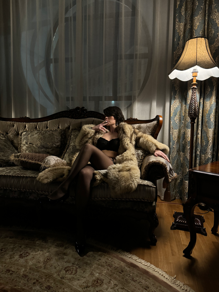 Woman in a fur coat and lingerie on an ornate sofa in a dimly lit room
