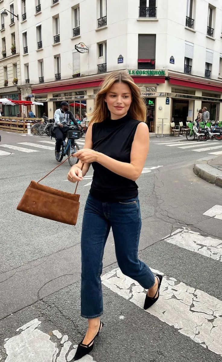 Woman in a black sleeveless top and jeans crossing a city street