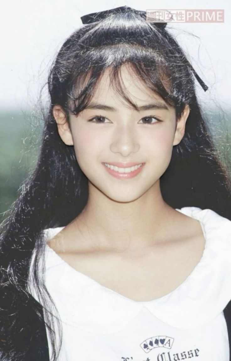 Young woman with long black hair and a black ribbon, smiling in a white top