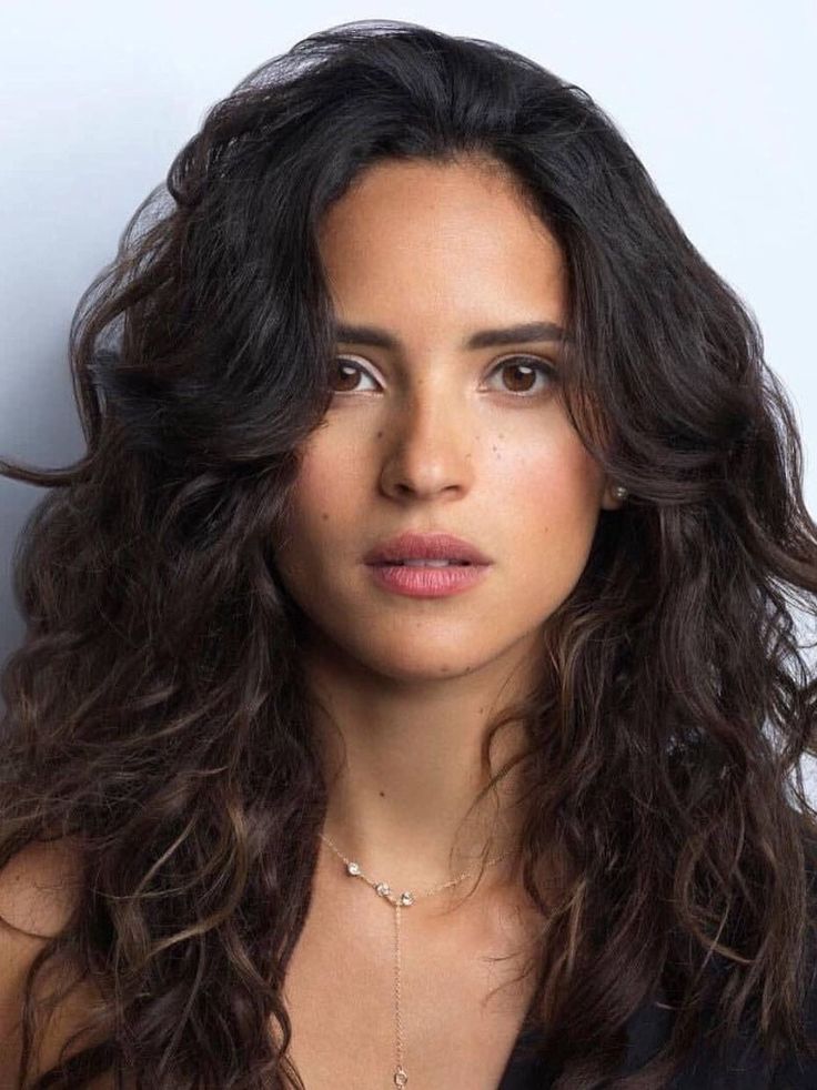 Woman with long dark hair and a delicate necklace looking directly at the camera