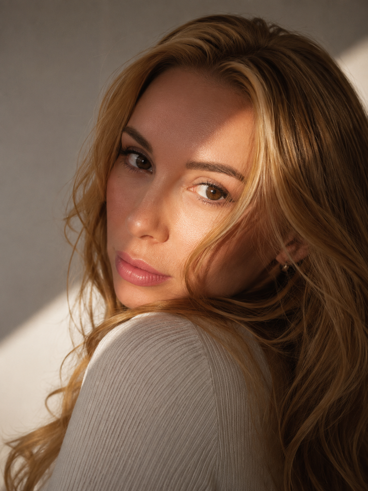 Woman with long blonde hair in soft, warm lighting looking over her shoulder