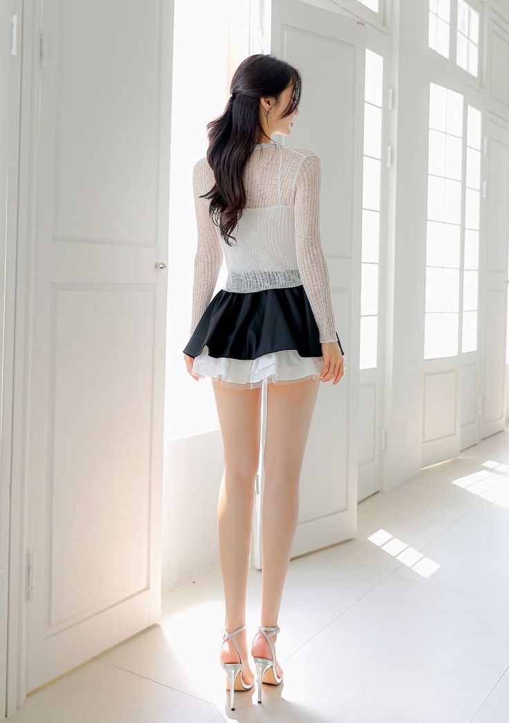 Woman in a sheer top and mini skirt standing indoors with soft lighting
