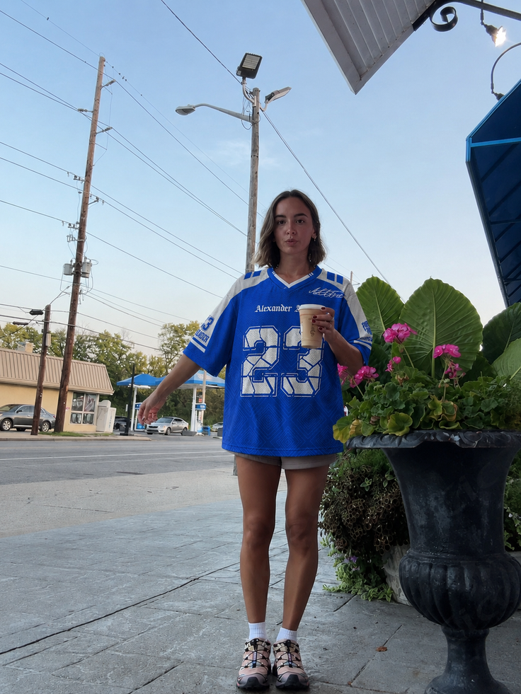 Woman in a blue jersey and shorts holding a cup on a street