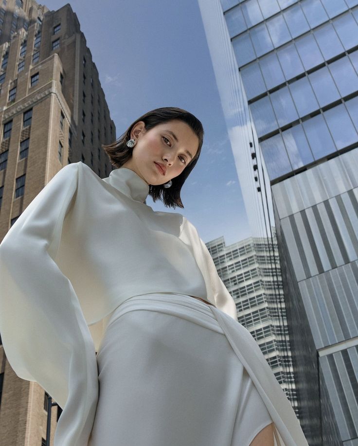Woman in a white dress with short hair posing in a cityscape