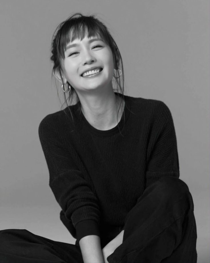 Woman with bangs and hoop earrings smiling in a black and white studio shot