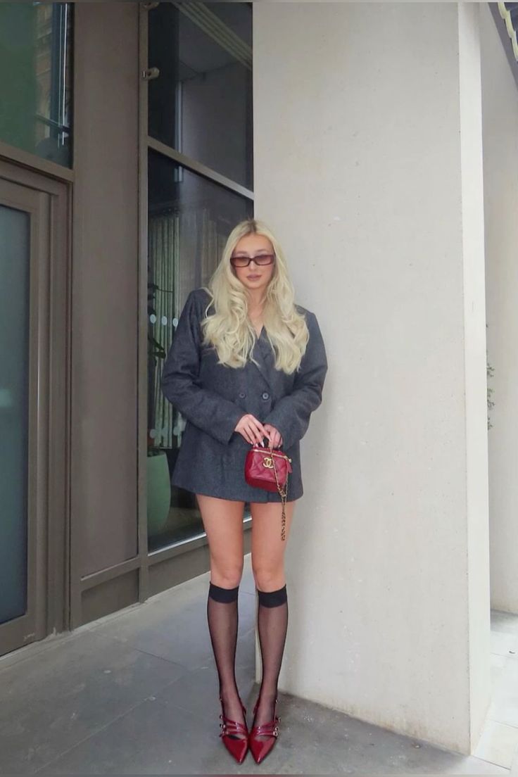 Woman with blonde hair wearing an oversized blazer, red heels, and knee-high socks