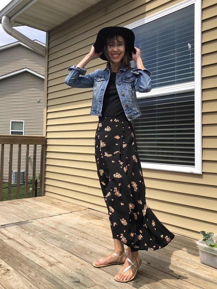 Woman in a denim jacket and floral skirt posing on a wooden deck