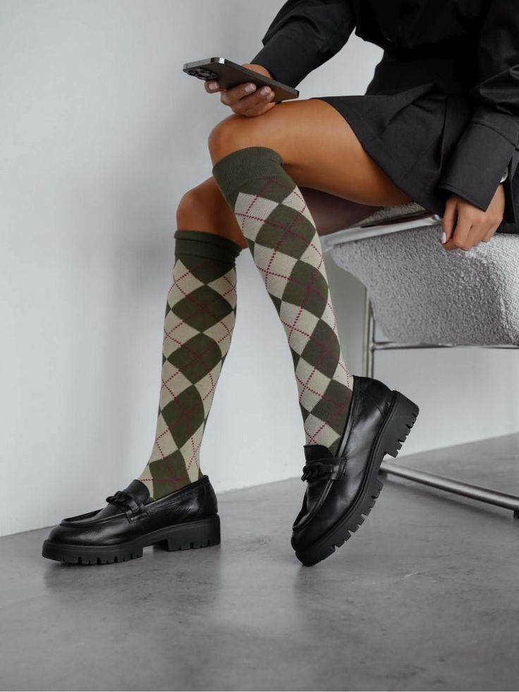Person wearing argyle socks and black loafers, sitting and holding a phone