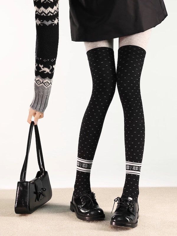 Person wearing a black skirt, patterned sweater, and over-knee socks with black shoes