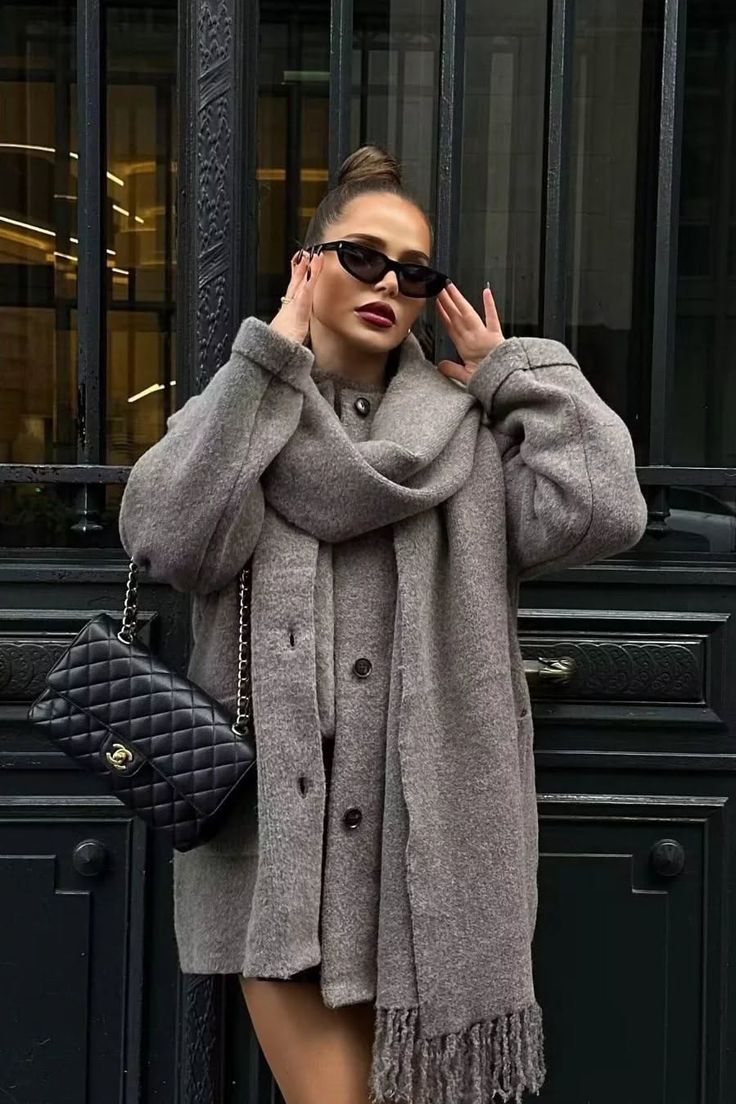 Woman in a gray coat and scarf with sunglasses and an updo