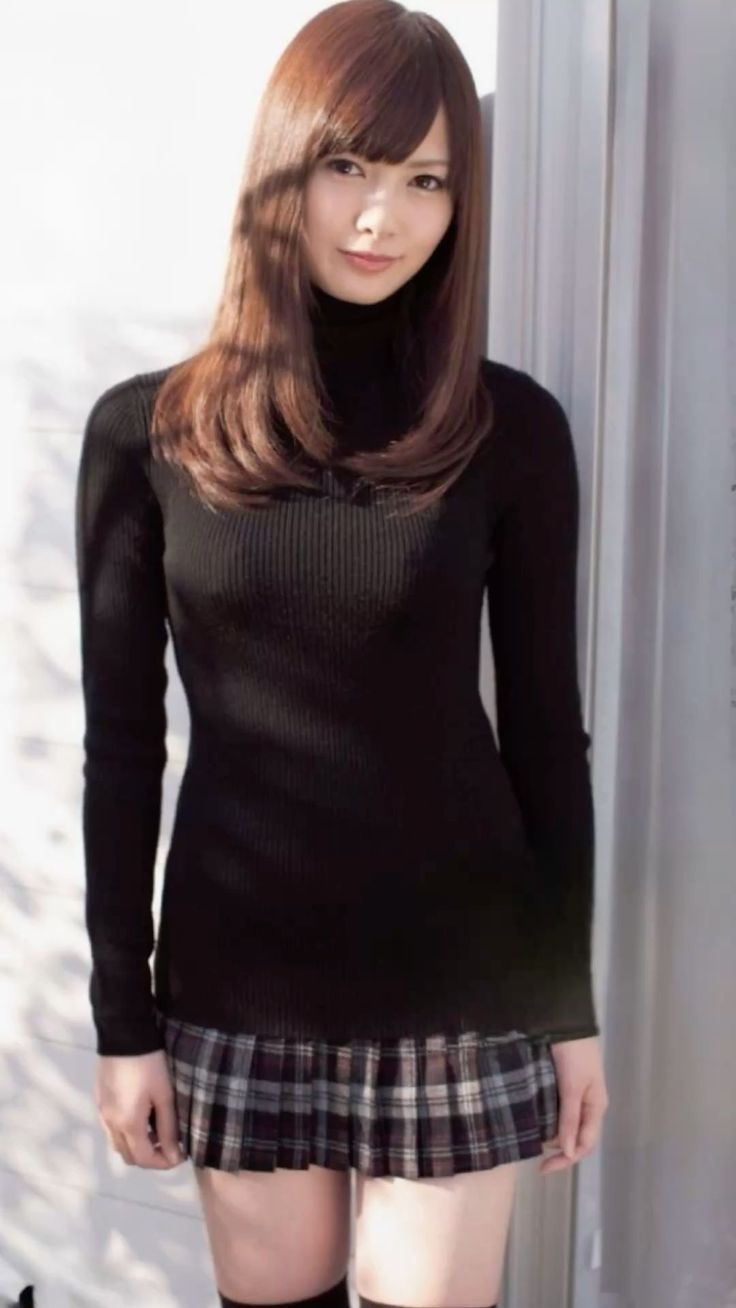 Woman with long brown hair wearing a black turtleneck and plaid skirt indoors