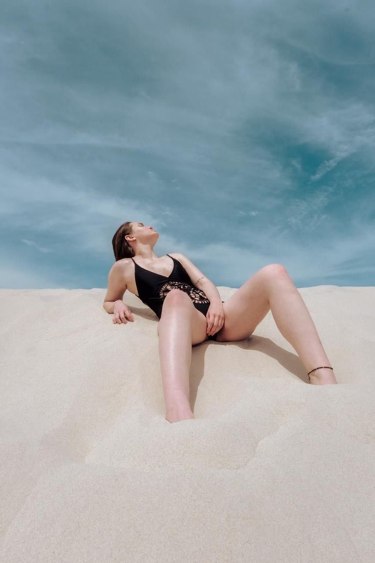 Woman in a black swimsuit lying on a sand dune under a blue sky