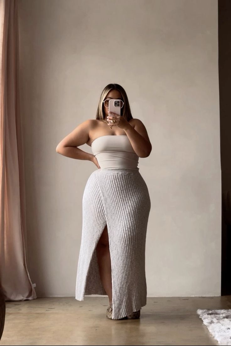 Woman in a strapless top and ribbed skirt with a high slit taking a mirror selfie