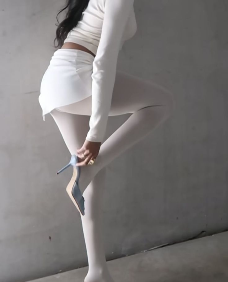 Woman in a white outfit and tights putting on a blue high heel shoe