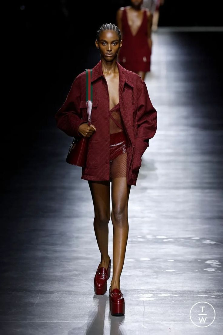 Model in a red outfit with platform shoes walking on a dark runway