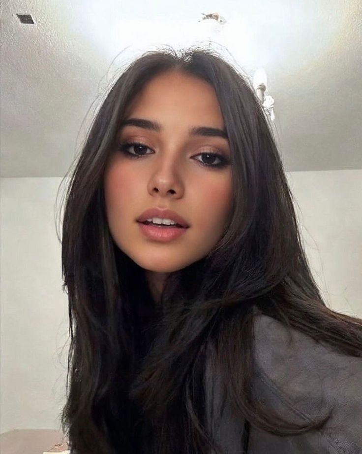 Woman with long dark hair looking directly at the camera indoors