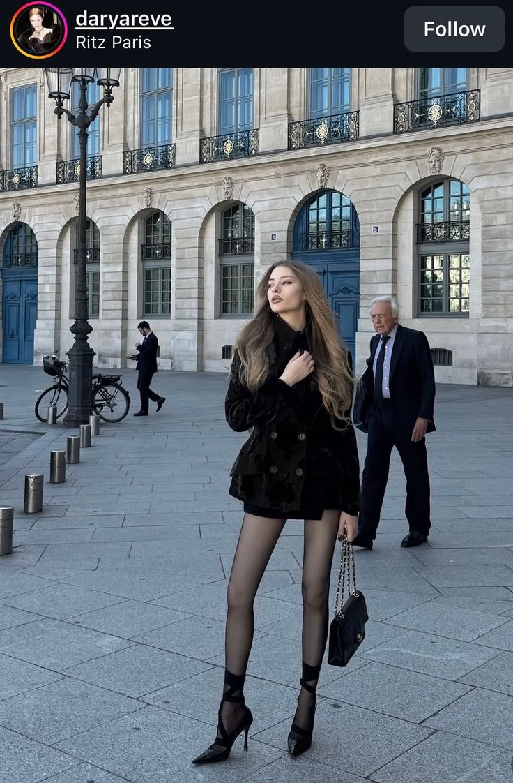 Woman in a black jacket and tights posing on a city street