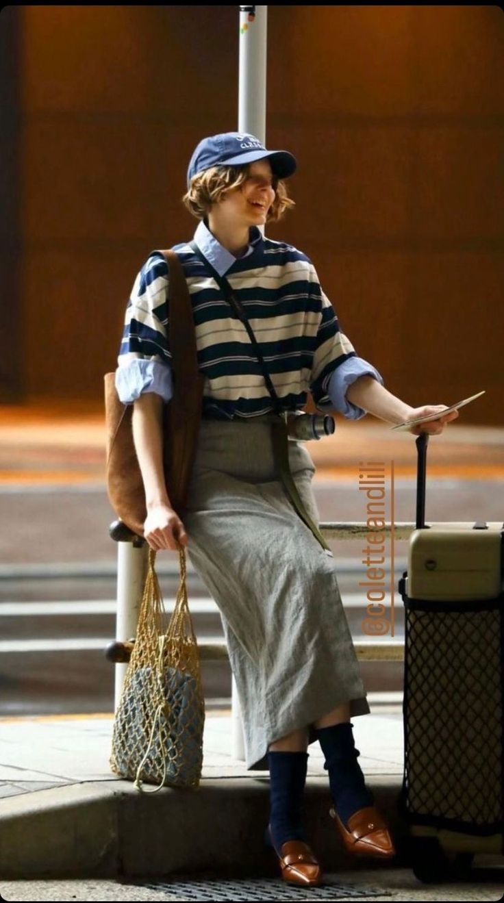 Person in a striped shirt and midi skirt with a baseball cap and luggage