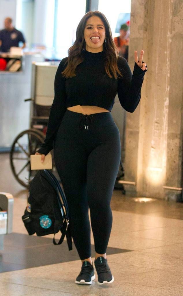 Woman in a black crop top and leggings making a playful face and peace sign