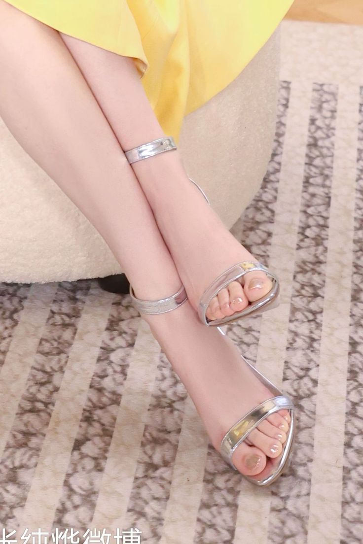Close up of bare legs and feet in silver high heels with a yellow dress