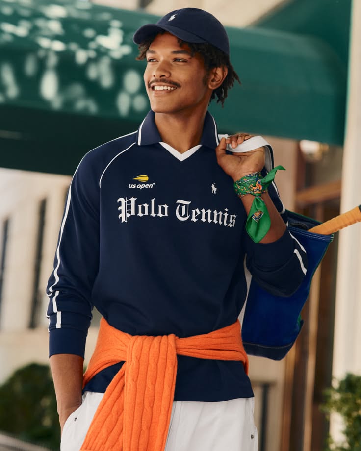 Man in a navy blue tennis shirt and cap, with an orange sweater tied around his waist