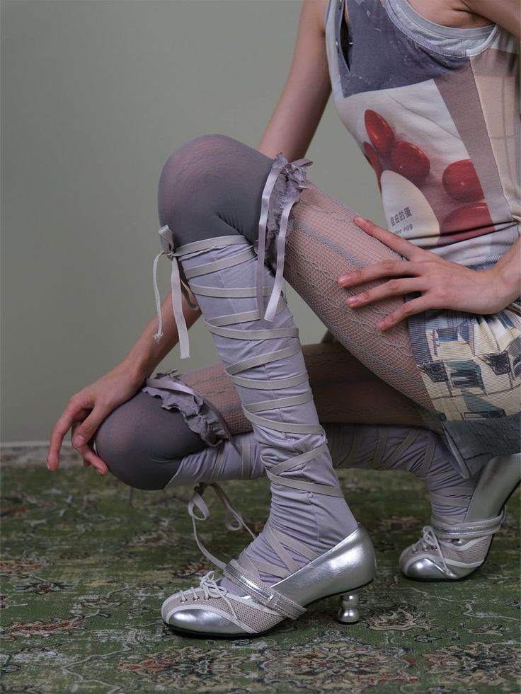 Person in silver shoes, fishnet stockings, and leg warmers squatting on a green carpet