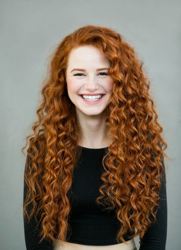 Woman with long curly red hair smiling in a studio portrait