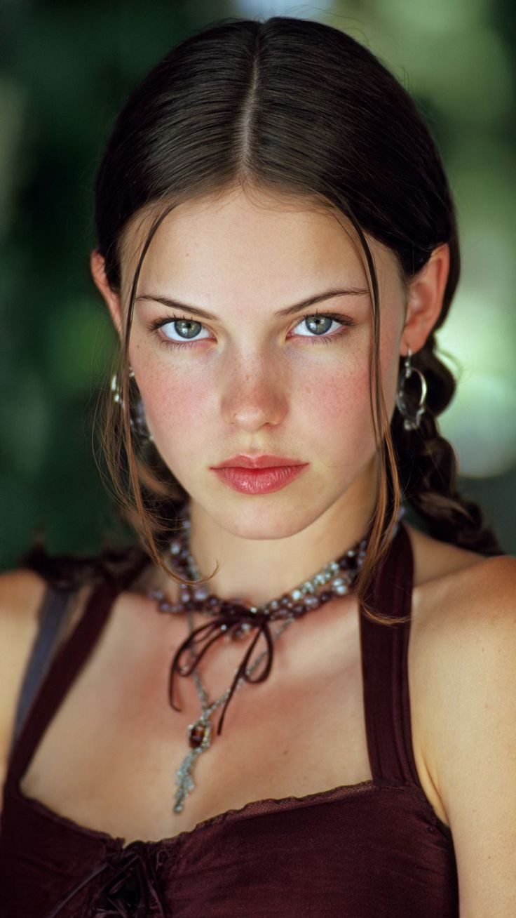 Woman with dark hair and freckles wearing a maroon top and necklace
