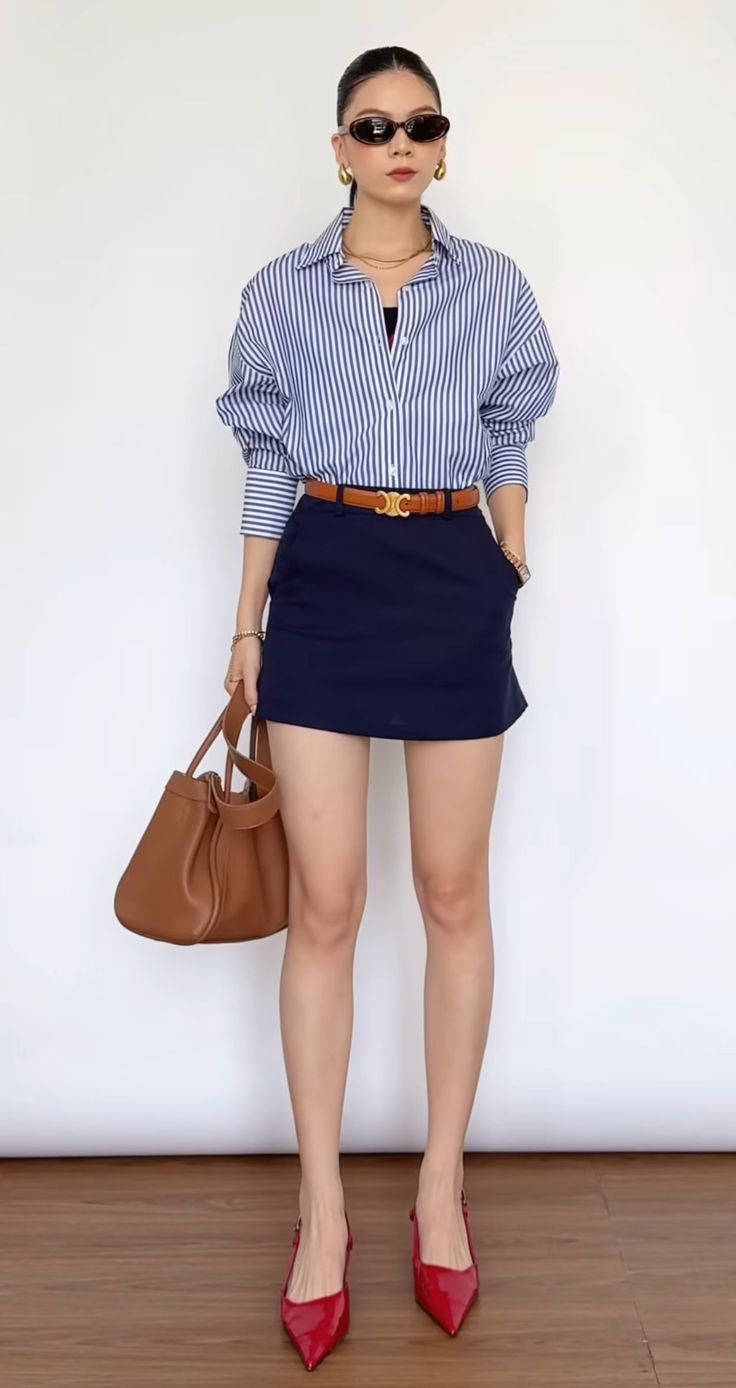 Woman in a striped shirt, navy mini skirt, and red heels holding a brown handbag