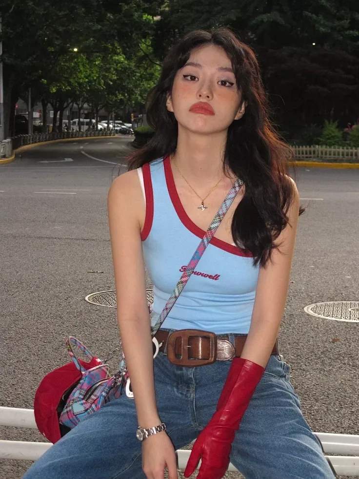 Woman with long dark hair wearing a blue tank top and red gloves on a street