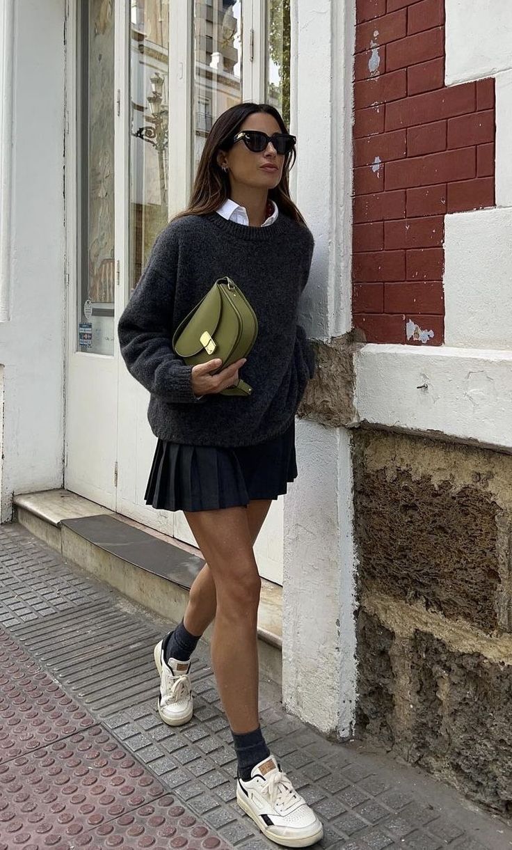 Woman in a sweater and pleated skirt with a green handbag walking outdoors