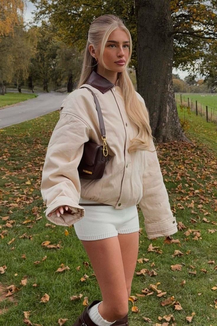 Woman with blonde hair in a puffer jacket and white shorts outdoors with autumn leaves