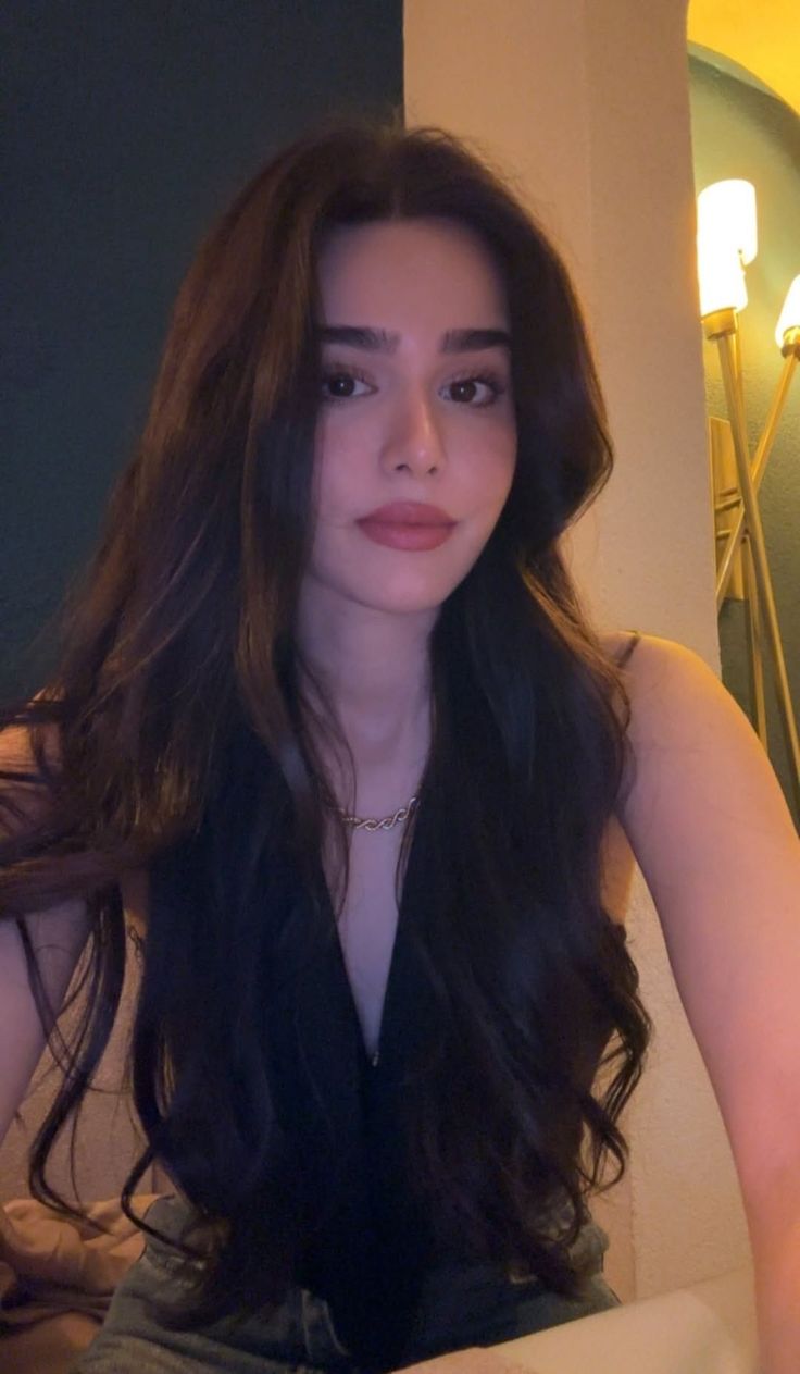 Woman with long dark hair wearing a deep v-neck top and gold necklace indoors