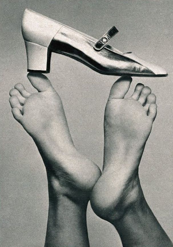 A high heel shoe balanced on a bare foot, with another foot in the background