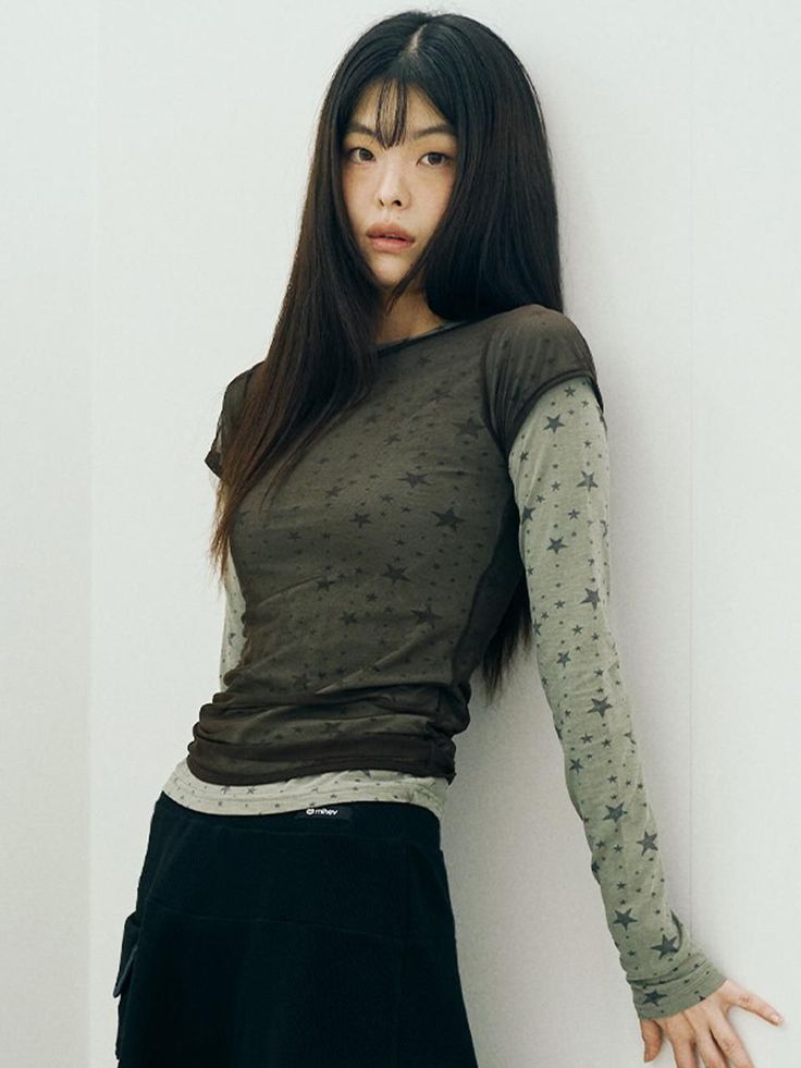 Woman with long dark hair and bangs wearing a star print layered shirt and black skirt
