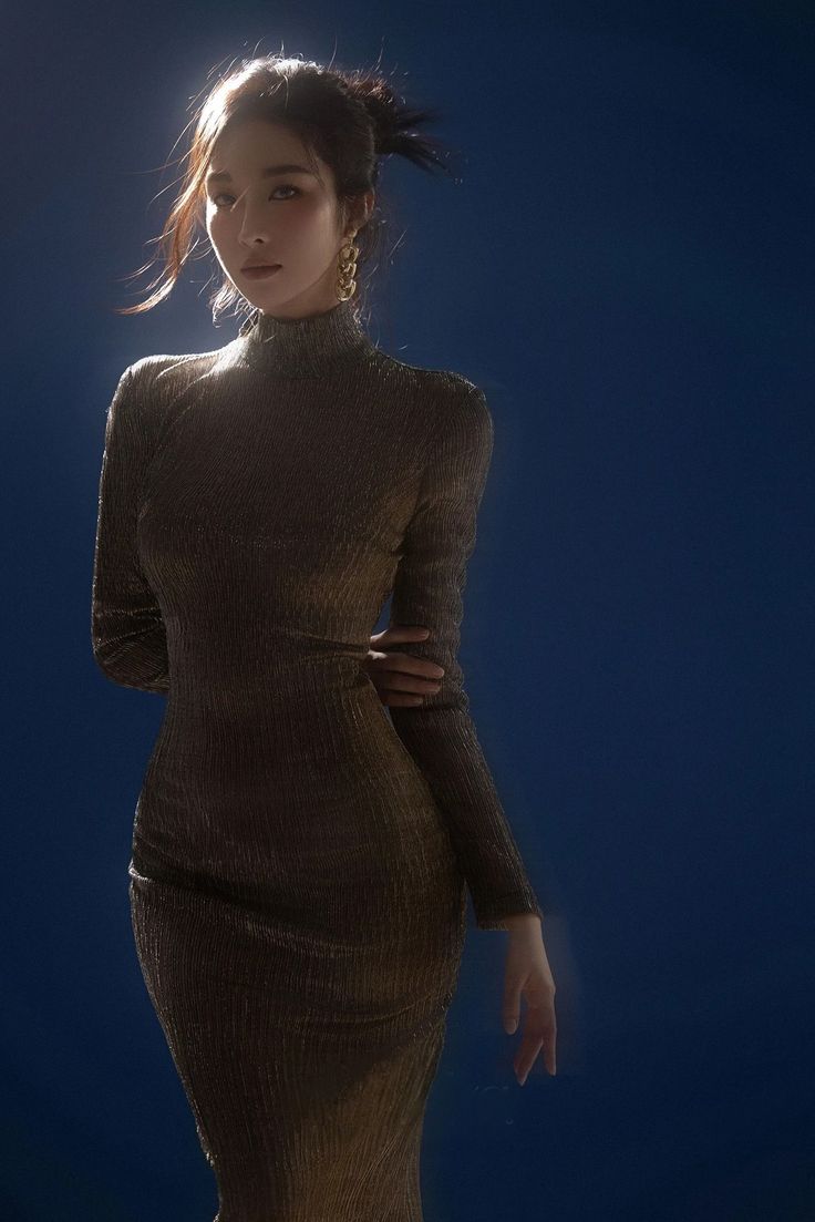Woman in a long gold dress with an updo hairstyle against a dark blue background
