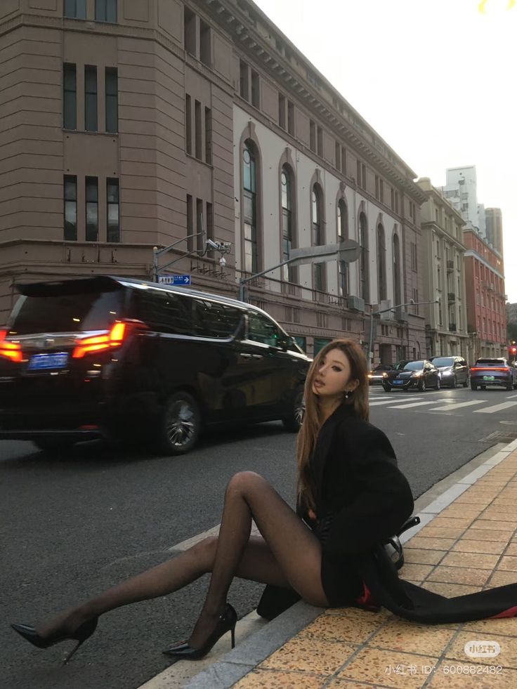 Woman in a black blazer and sheer stockings sitting on a city curb