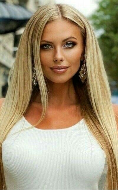 Woman with long blonde hair and blue eyes wearing a white top and earrings