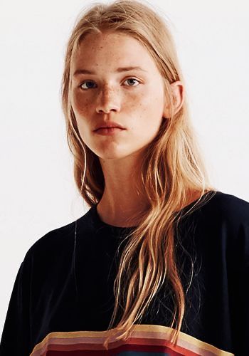 Woman with blonde hair and freckles wearing a black t-shirt with colorful stripes