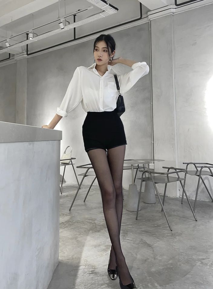 Woman in a white shirt and black shorts with pantyhose posing indoors