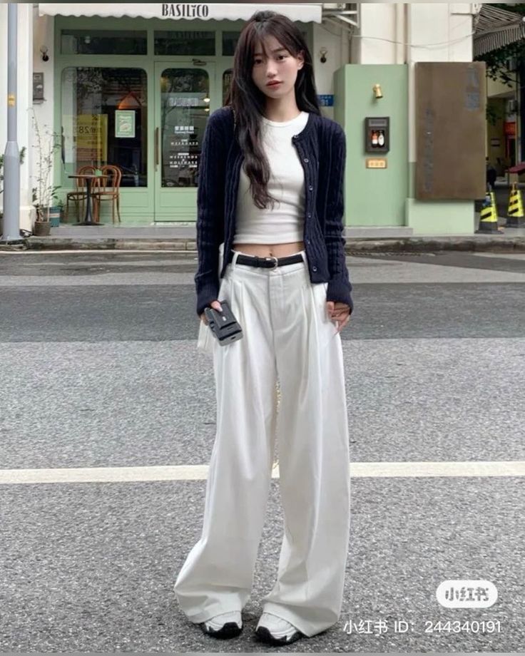 Woman in a black cardigan and white wide leg pants on a street