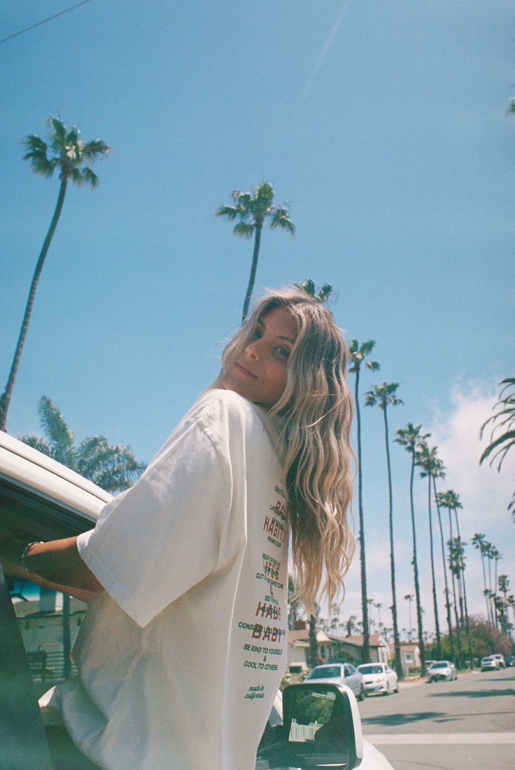 Woman with long blonde hair in an oversized t-shirt on a street with palm trees