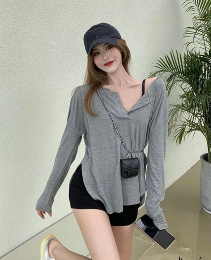 Woman in a gray long-sleeve shirt and black shorts with a baseball cap