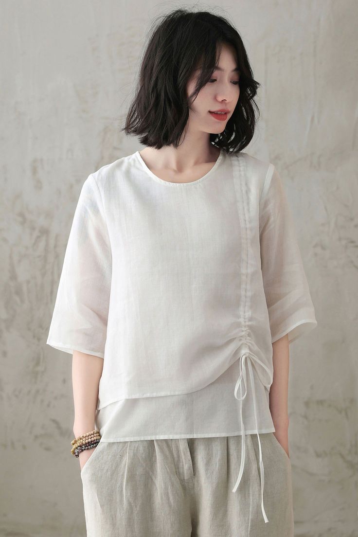 Woman with short dark hair wearing a white top and linen pants