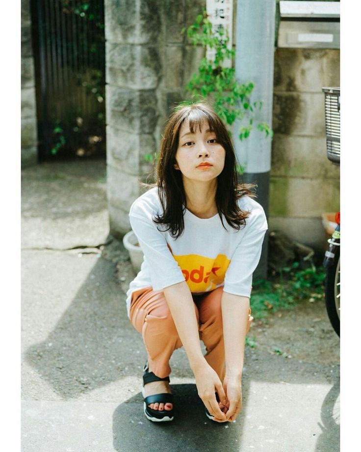 Woman in a white t-shirt and orange pants crouching outdoors