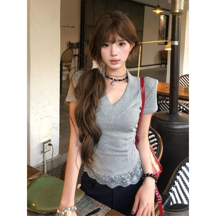 Woman with a long ponytail wearing a gray top with lace trim and a choker indoors