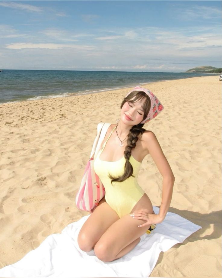 Woman in a yellow swimsuit and head scarf kneeling on a beach